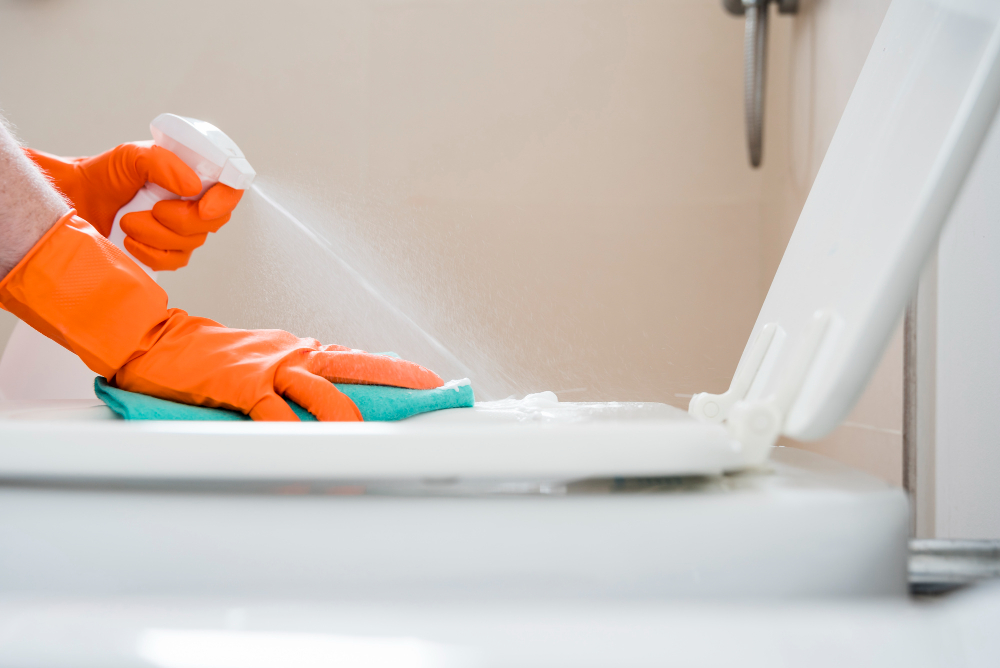 an  image of a perosn wearing an orange gloves while cleaning the toilent